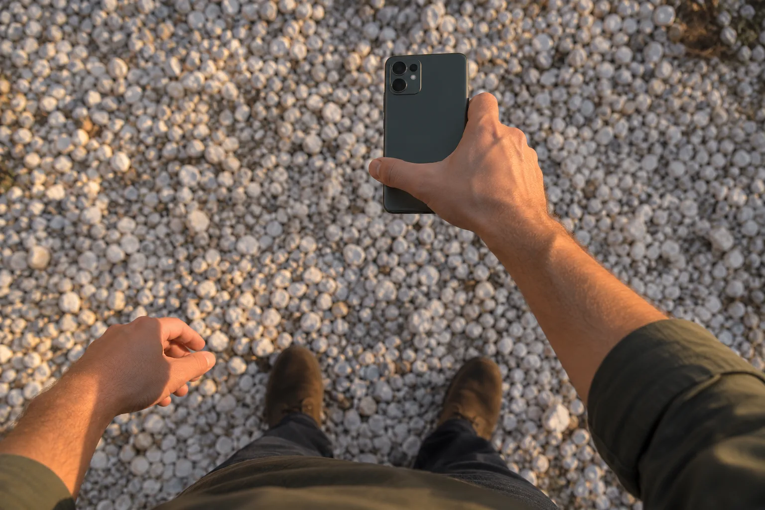 A hand reaching out over gravel holding a smartphone. The person and phone are AI-generated illustrations