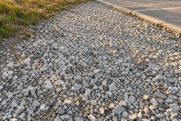 Trial 1, the shrunk whole photo: the white gravel strip between a grass edge and a parking lot, with the earbud not easy to see